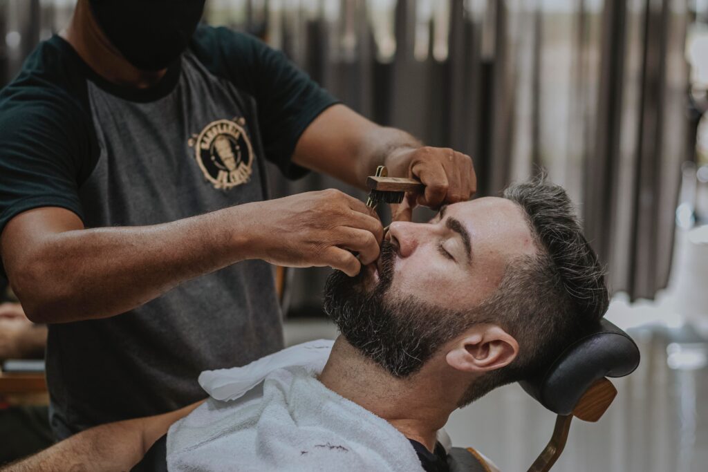 Photo by Carlos Magno man in black crew neck t-shirt cutting hair of man